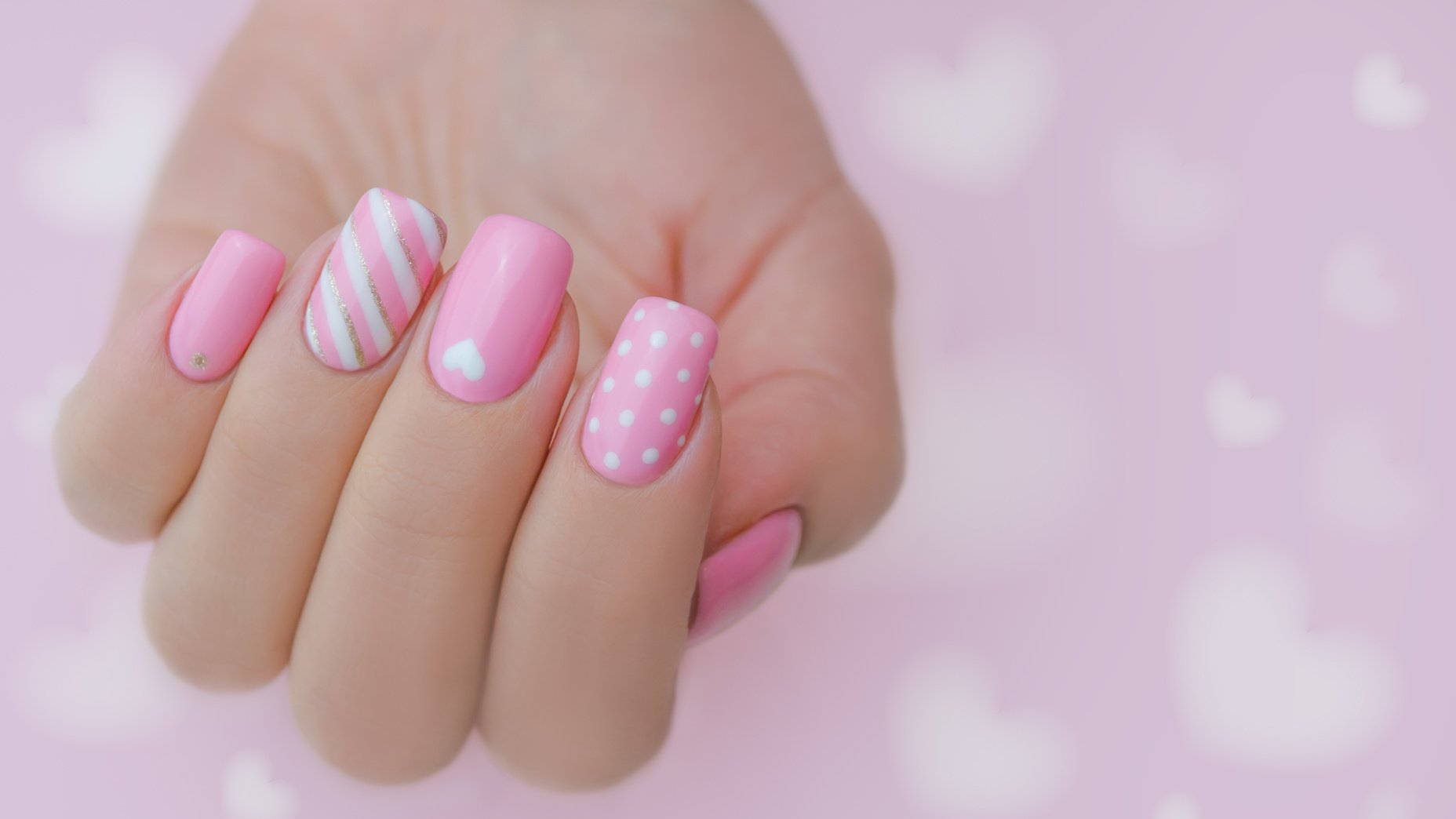 The hand of a young woman. The nails are covered with pink gel polish for Valentine's Day. Nail art and design ideas, heart.