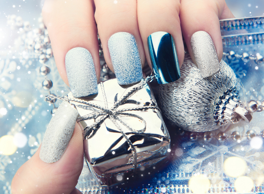 a hand with silver and blue nails holding a silver gift box
